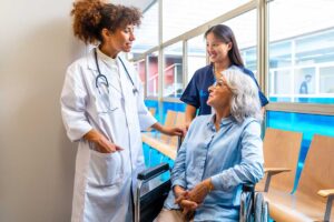 A social worker speaks privately with an older resident at a table beside a care plan folder.